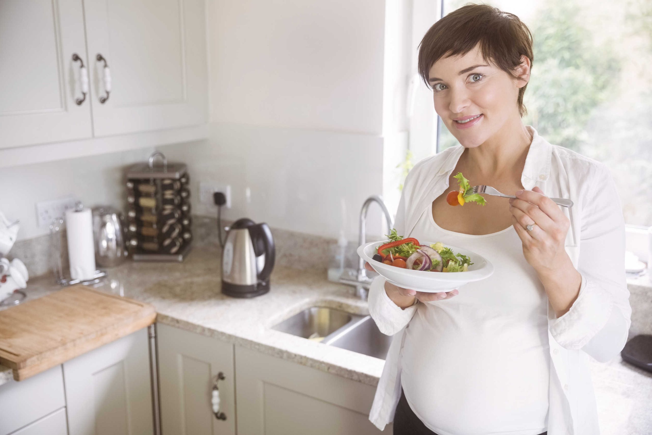 Pregnant woman having bowl of salad at home in the kitchen